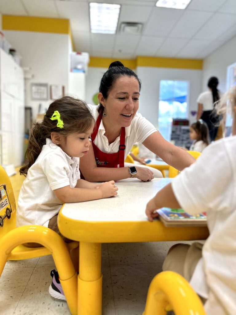 Pre-school teacher sitting with two toddlers on a white top table.