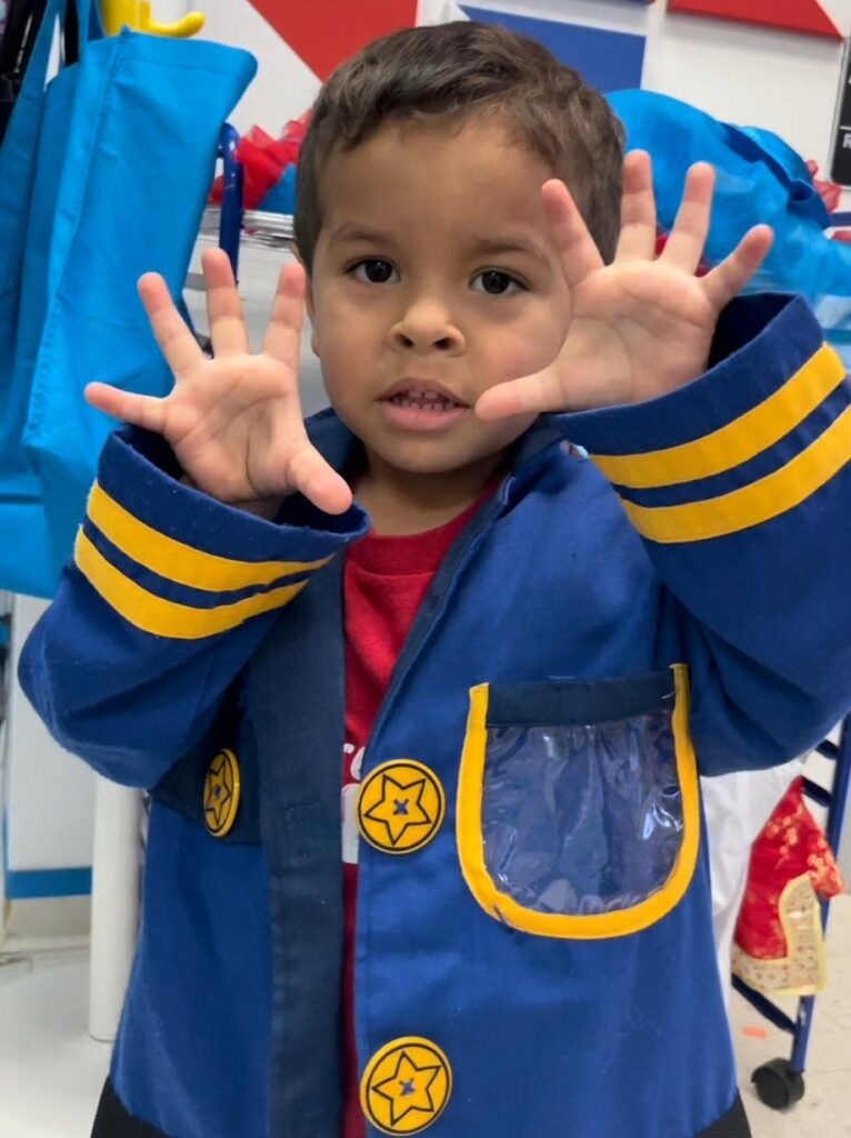 Toddler with both hands up presenting his hands, wearing a blue coat with yellow stripes